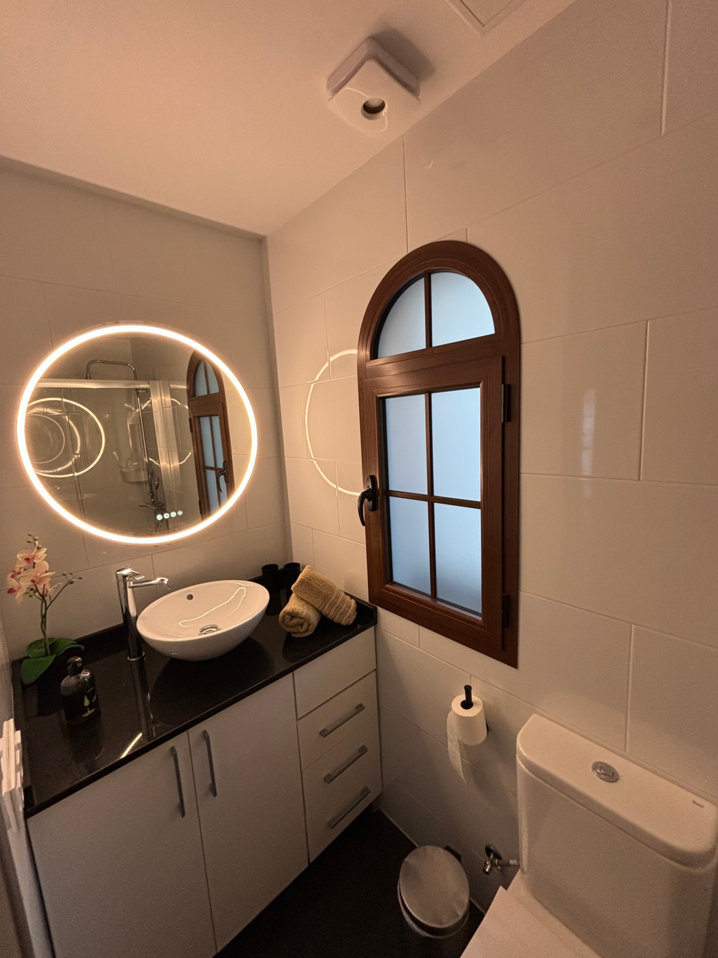 Bathroom vanity with washbasin, illuminated round mirror and arched window
