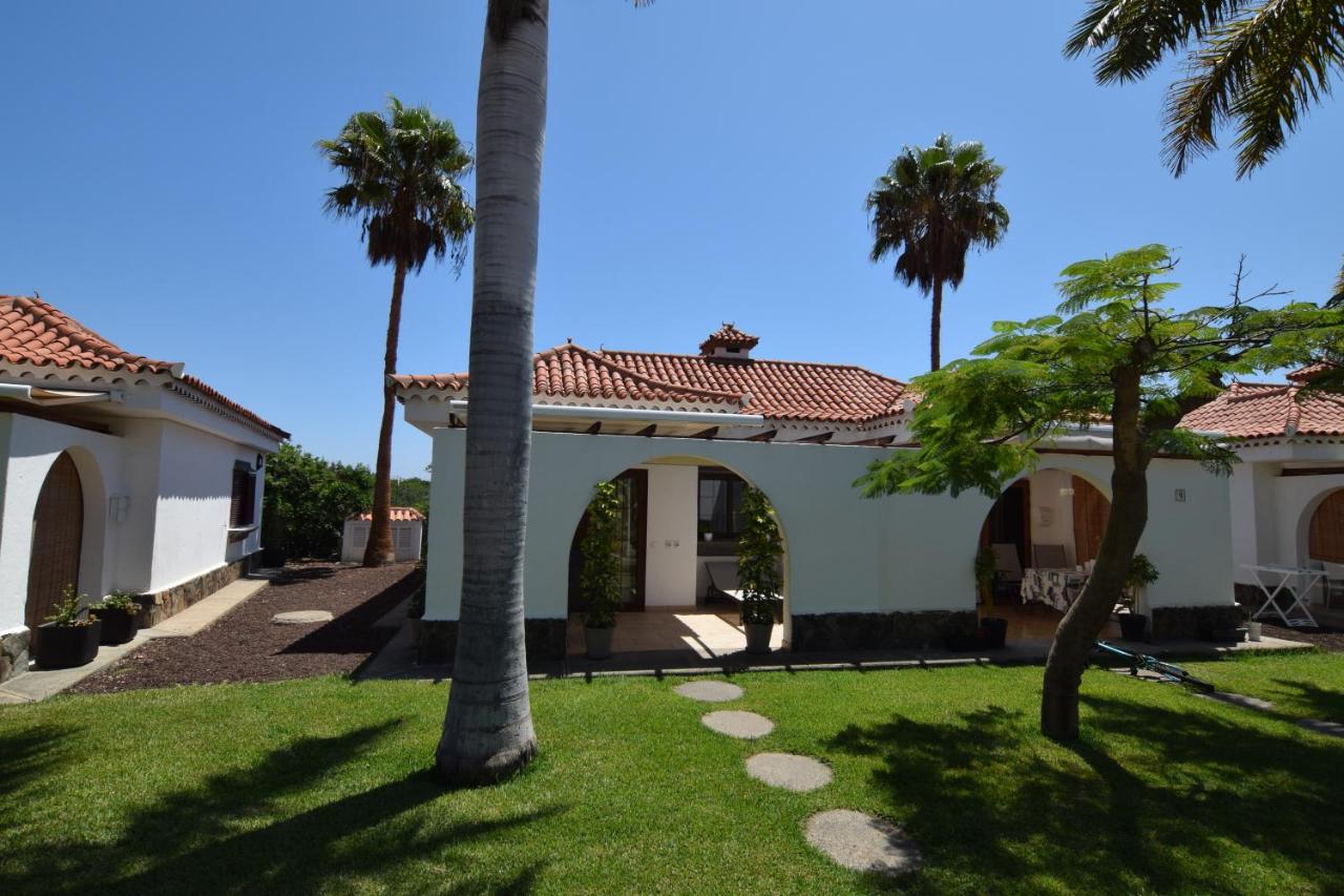 Exterior of the bungalow with terracotta roof, palm trees and lawned garden