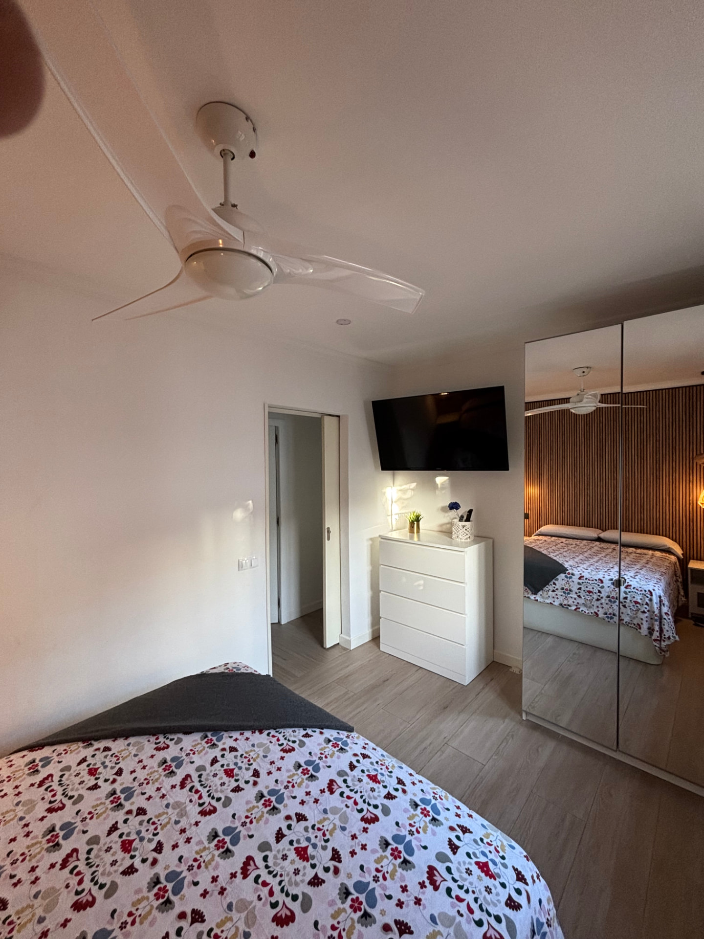 Bedroom seen from the doorway, with television, chest of drawers and mirrored wardrobe